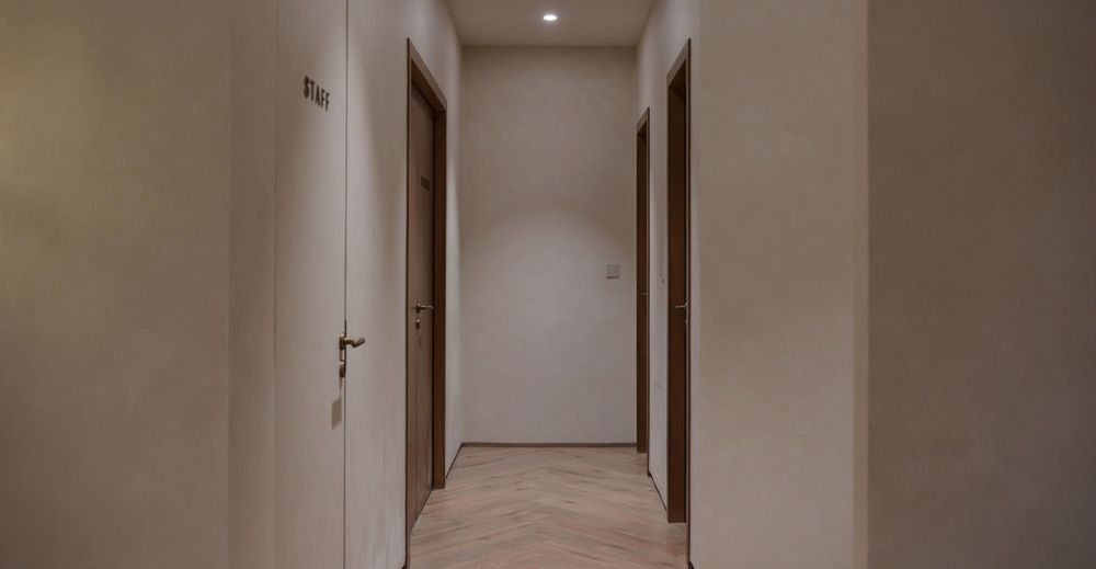 Interior photography of a minimalist hallway with wooden doors, grey walls, and warm ambient lighting, creating a serene and professional atmosphere.